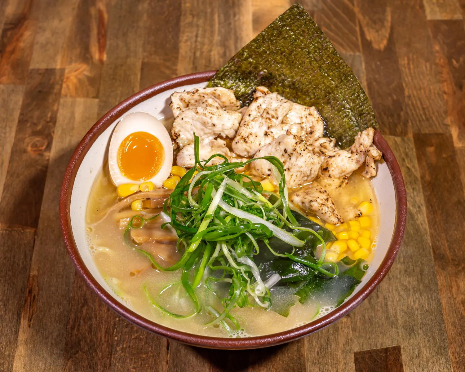 Chicken Ramen bowl with grilled chicken, a soft-boiled egg, bamboo shoots, corn, scallions, and nori in broth
