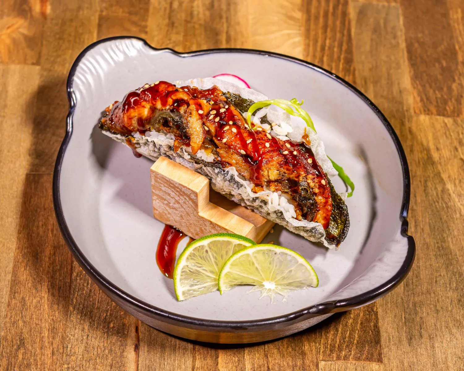 Eel Sushi Taco filled with grilled eel and rice, drizzled with eel sauce and sesame seeds, served with lime wedges
