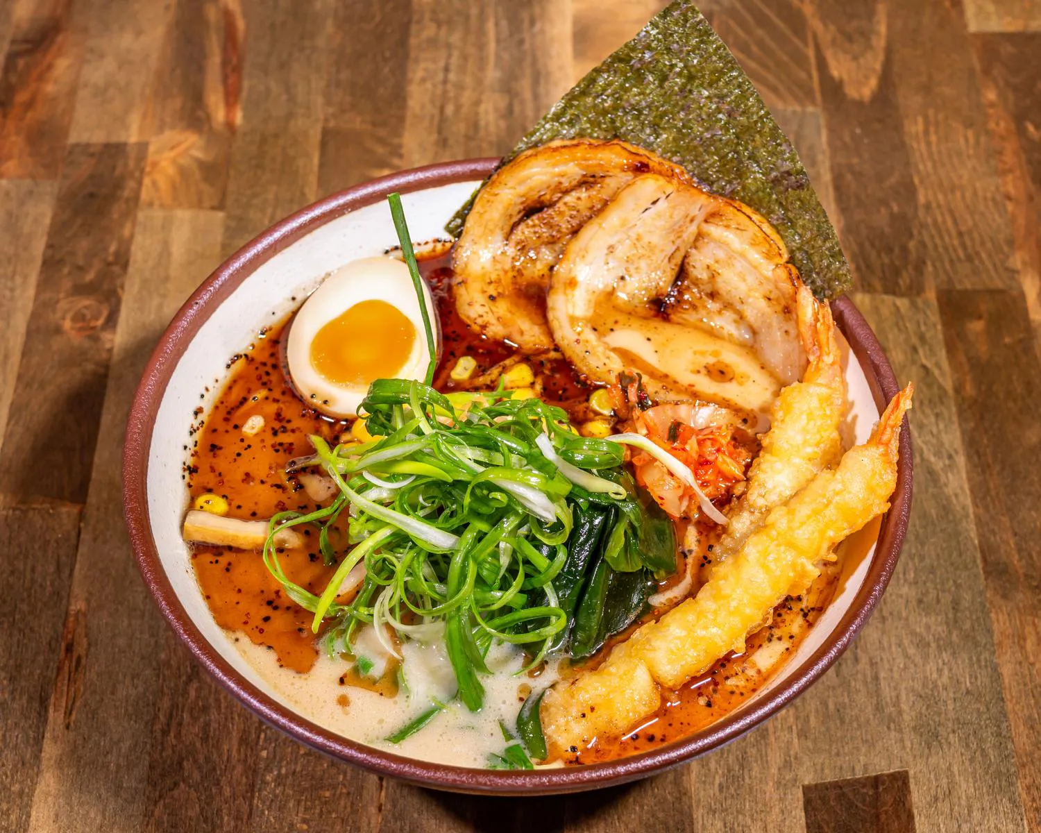 Mega Ramen bowl topped with sliced pork chashu, tempura shrimp, a soft-boiled egg, kimchi, scallions, corn, and nori