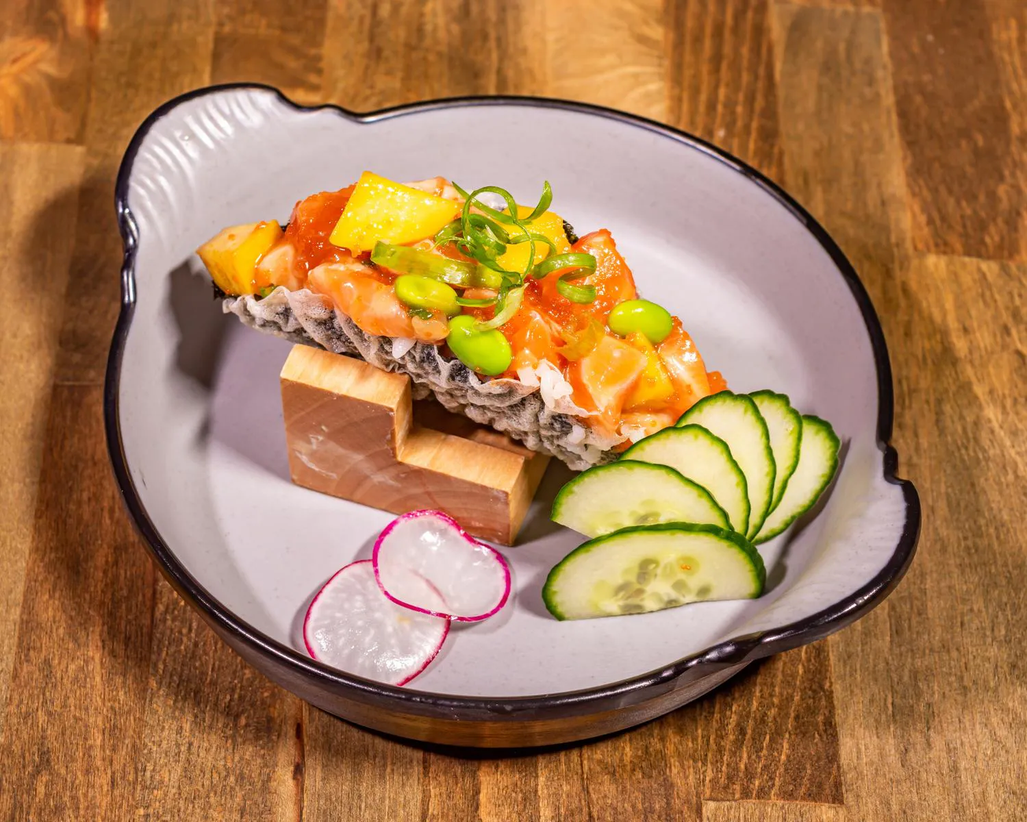 Salmon Sushi Taco filled with diced salmon, mango, edamame, and scallion, served with cucumber and radish slices