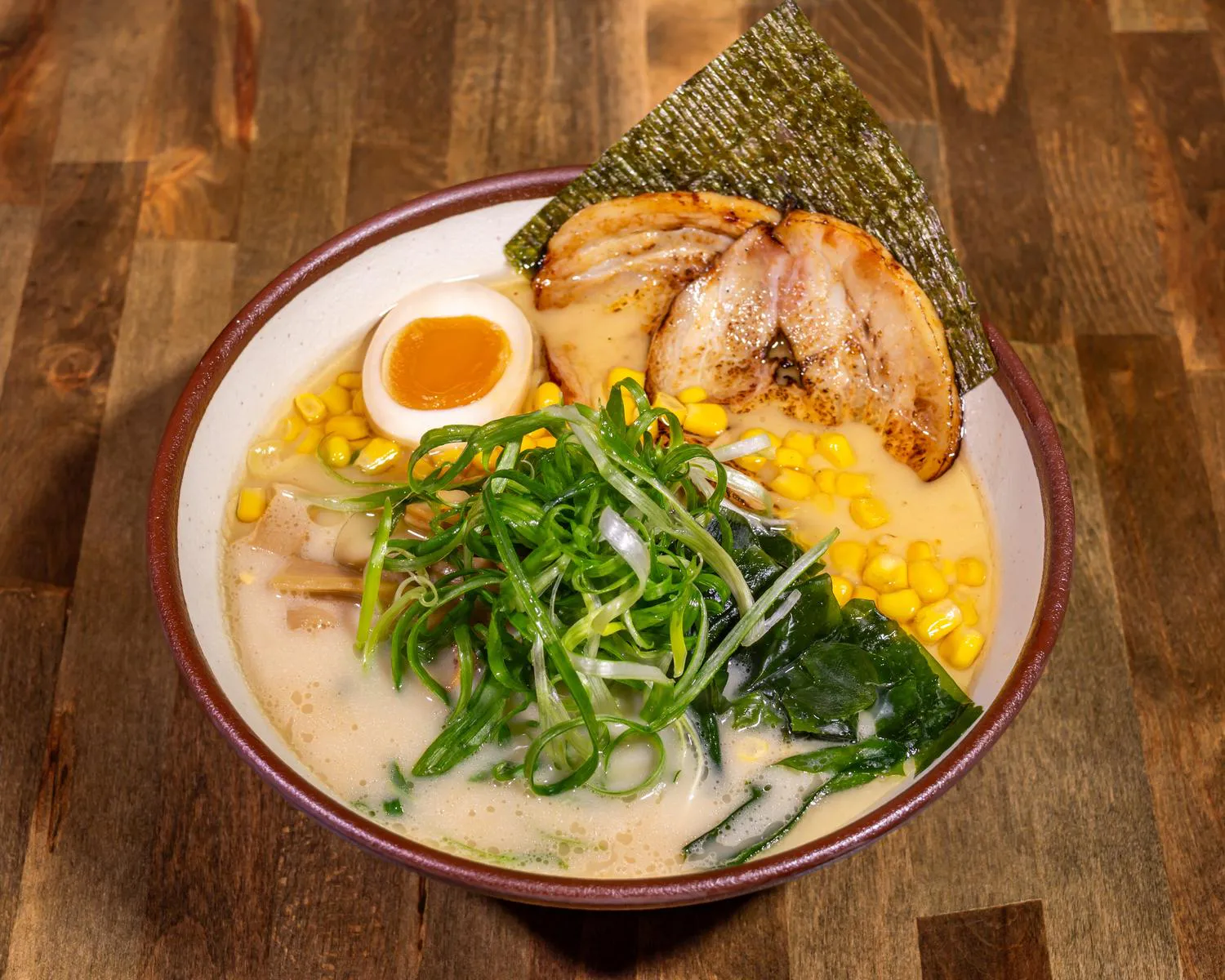 Tonkotsu Ramen bowl with sliced pork chashu, a soft-boiled egg, corn, bamboo shoots, scallions, and nori in white garlic broth